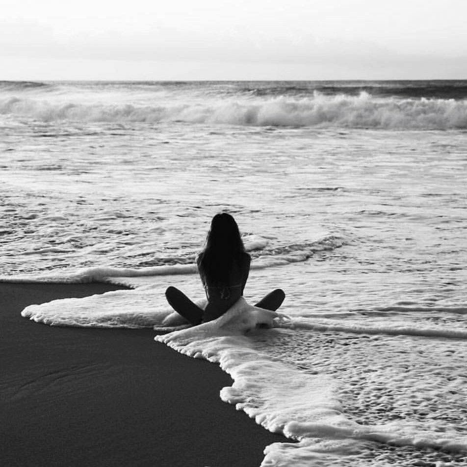 A woman sitting from behind at the ocean's edge as the surf rolls in